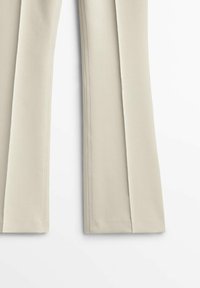 Pantalons plissés beiges en tissu lisse, avec une coupe droite et des ourlets soigneusement finis. Design minimaliste sans motifs visibles.