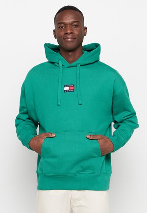 Vihreä huppari, joka on valmistettu teksturoidusta kankaasta, jossa on etupuolella kengurulaukku ja pieni logo-ompelu erivärisinä.