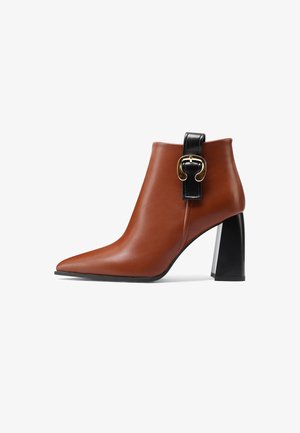 Stivale alla caviglia in pelle marrone con punta appuntita, dettaglio in pelle nera e finiture dorate, suola chunky nera.