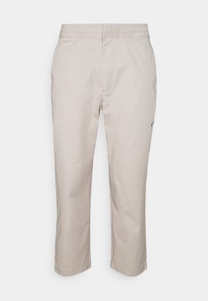 Pantalon beige clair à jambes droites avec un devant lisse, des poches latérales et une taille ajustée, présenté sur un fond uni.