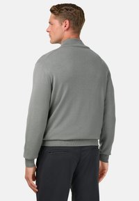 Šedý pletený svetr s vysokým límcem, žebrovanými manžetami a zakončením. Zobrazen zezadu, odhalující hladkou texturu a přiléhavý střih.