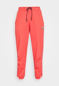Coral joggers with elastic waistband, adjustable drawstring, two side pockets, and white accents at cuffs. Made from soft, textured fabric.