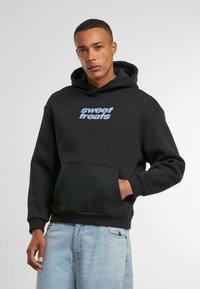 Black hoodie made of soft fabric, featuring a front kangaroo pocket and blue text "sweet treats" centered on the chest.