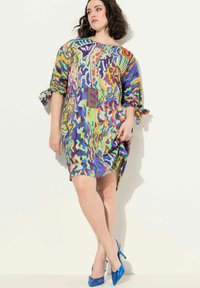 Monivärinen tunikamekko, jossa on abstrakteja kuvioita, löysä istuvuus, keskipitkä pituus ja kääntöhiat. Yhdistettyinä sinisiin kärkinuoriin.