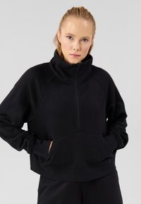 Mustast fliisist pullover kõrge krae ja poole lukuga sulgemisega. Omadusteks on kengurutasku ja soonikkoes varrukasääred. Pehme tekstuur, mugav lõige.