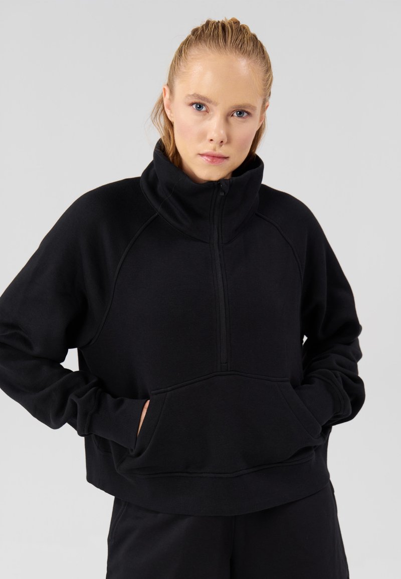 Mustast fliisist pullover kõrge krae ja poole lukuga sulgemisega. Omadusteks on kengurutasku ja soonikkoes varrukasääred. Pehme tekstuur, mugav lõige.