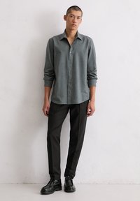 Grijs button-up shirt met een gestructureerd patroon, gecombineerd met zwarte slim-fit broeken en zwarte veterschoenen, voor een effen achtergrond.