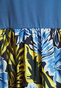 Haut en tissu bleu attaché à une jupe froncée avec un motif botanique multicolore en jaune, vert, noir et nuances de bleu.