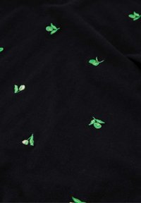 Zwarte stof met verspreide groene geborduurde bladeren en knoppen, wat textuur en een natuurlijk patroon aan het materiaal toevoegt.