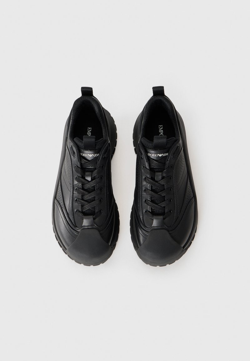 Svarta träningsskor med slätt läder och mesh-översida, rund tå, tjock gummisula och kontrasterande sömdetaljer.