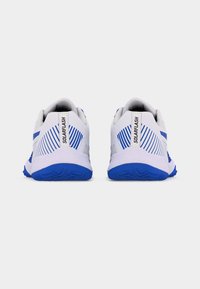 Ζευγάρι λευκών και μπλε αθλητικών παπουτσιών με την επιγραφή «SOLARFLASH» στις ταμπέλες της φτέρνας, σε απλή λευκή φόντο, από πίσω.