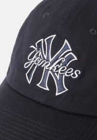 Mornarska kapa s vizirkom, s izvezenim bijelim i sivim "NY" logom i tekstom "Yankees". Ima zakrivljeni vizir i teksturiranu tkaninu.