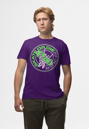 Lila T-Shirt mit kurzen Ärmeln und einem Frontdruck mit dem Text "SKATE OR DIE" in Grün, der Skelethände zeigt, die ein Skateboard greifen.