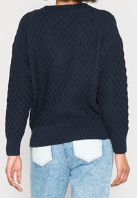 Mörkblå stickad tröja med strukturerat diamantmönster, ribbade ärmslut och nederkant, samt sänkt axelsöm, sedd bakifrån.