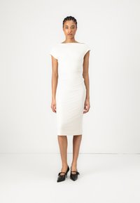 Form-fitting white dress with short sleeves and boat neck; smooth texture, knee-length, paired with black high-heeled shoes.