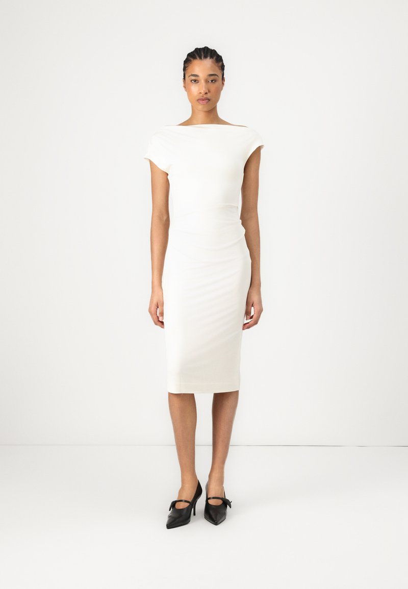 Robe blanche ajustée avec des manches courtes et un col bateau ; texture lisse, longueur au genou, associée à des chaussures à talons hauts noires.