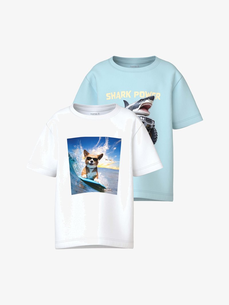 Λευκό μπλουζάκι με σκύλο που φοράει γυαλιά ηλίου και σερφάρει σε κύμα· ανοιχτό μπλε μπλουζάκι με καρχαρία και τον κείμενο "SHARK POWER" πάνω από ένα τερατότροχο φορτηγό.