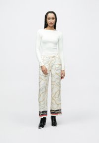 Top alb cu mâneci lungi, cu dungi și croială strânsă, asortat cu pantaloni largi, cu model cu lanțuri aurii și bordură contrastantă. Cizme negre cu toc.