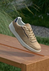 Beige mockaskor med vit gummisula, rund tå och kontrasterande marinblå accenter längs sömmarna och ögonen. Perforerat tådetalj.