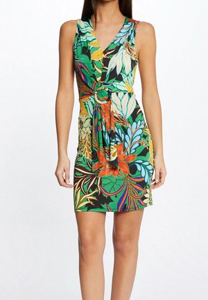 Woman wearing sleeveless, knee-length dress with colorful tropical floral pattern and a fabric belt with a round buckle at the waist.