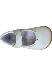 Zapato Mary Jane de cuero blanco con punta redonda y correa, que presenta patrones de corazones recortados y una suela de goma marrón claro.