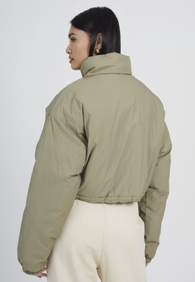 Chaqueta de plumas recortada en verde oliva con cuello alto, mangas oversize y dobladillo elástico. Textura suave y detalles de costura mínimos.