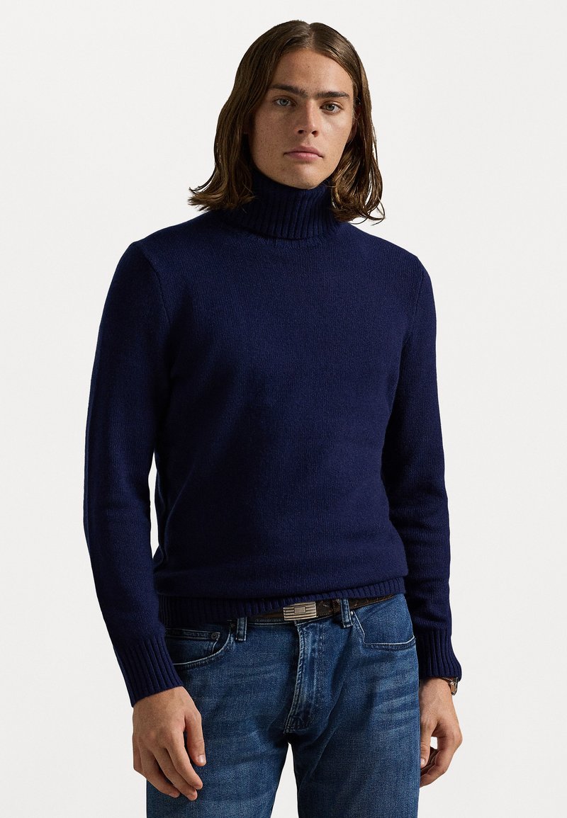Pulover de culoare albastru marin, cu guler înalt, realizat dintr-un tricot texturat, având mansete și tiv cu nervuri. Asortat cu blugi, evidențiați de o curea.