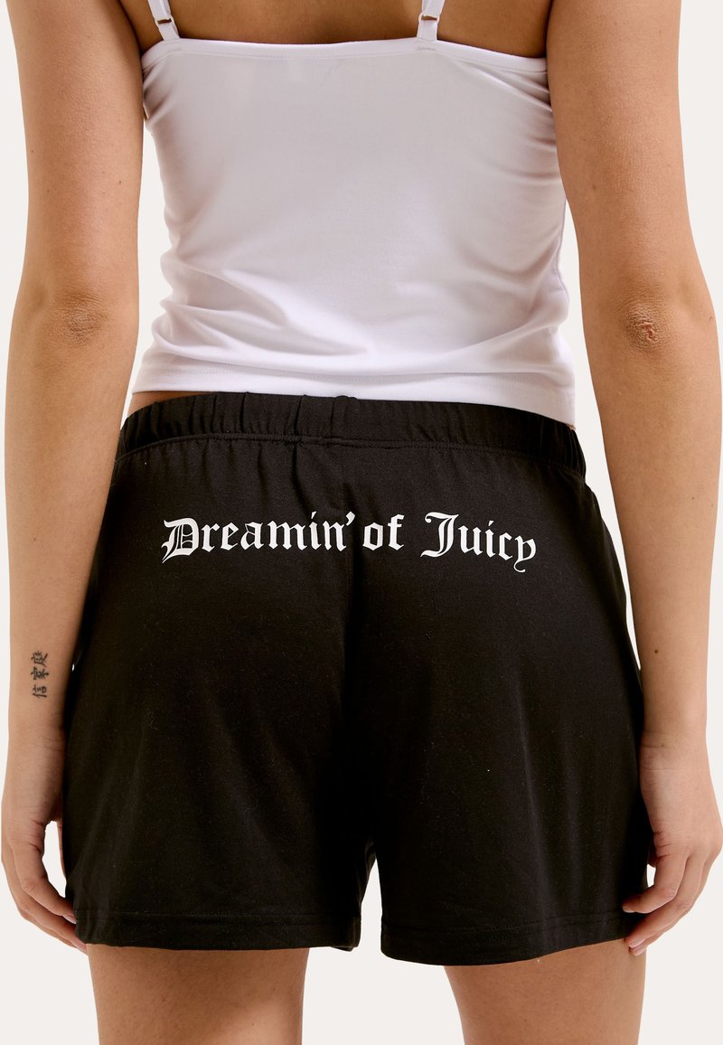Pantaloni corti neri in cotone, con una vita elasticizzata e la scritta bianca "Dreamin’ of Juicy" stampata sul retro. Design e vestibilità semplici.