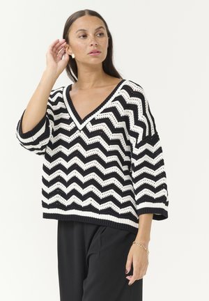 Black and white chevron-patterned knit sweater with a V-neck, loose fit, three-quarter sleeves, and ribbed hem. Textured fabric.
