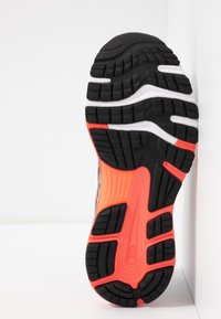 Suela de zapatilla de correr negra y naranja con goma texturizada, surcos profundos para tracción y un acento naranja vibrante alrededor del talón.