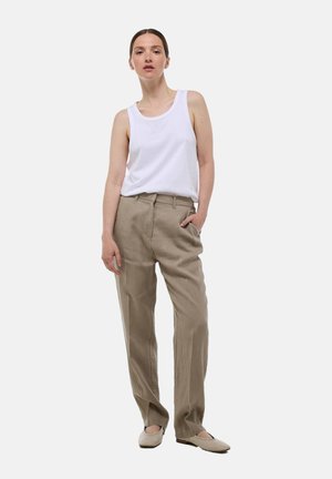 Débardeur blanc sans manches associé à un pantalon en lin beige, offrant une coupe décontractée et des poches avant, porté avec des chaussures plates beiges.