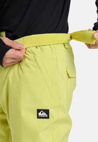 Geel sneeuwbroek met een verstelbare tailleband met klittenband, zijzakken en een zwart Quiksilver logo op de heup.