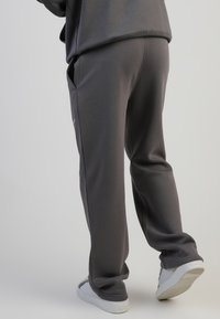 Szürke jogger nadrág puhával készült anyagból, egyenes szabással, rugalmas derékkal és oldalsó zsebekkel. Fehér sportcipővel párosítva.