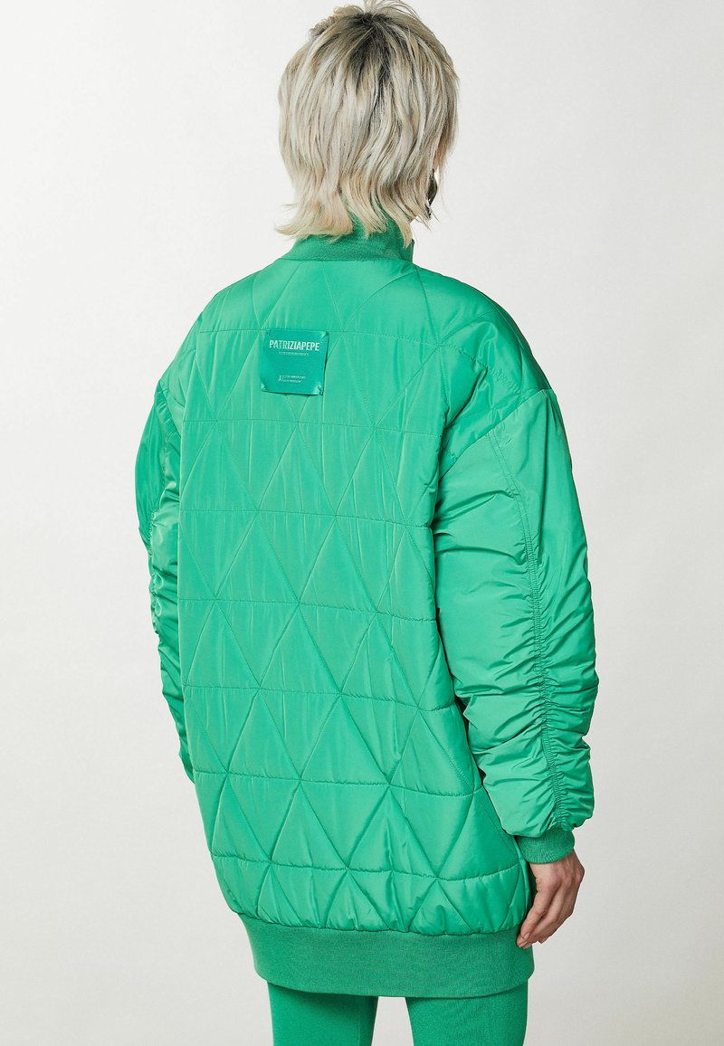 Zielona pikowana kurtka puchowa o luźnym kroju, z wzorem w romby, ściągaczami na rękawach oraz metką z tyłu. Gładki, błyszczący materiał.