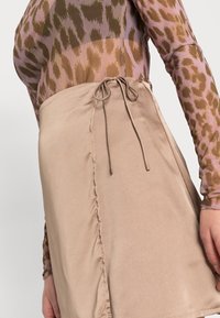 Satinbeige minikjol med rynkdetaljer, sidoförslutning och en mjuk textur. Kombinerad med en långärmad mönstrad topp.