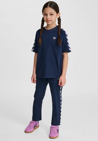 Completo sportivo blu navy composto da una t-shirt a maniche corte e pantaloni abbinati con strisce bianche sui lati. Le scarpe sono rosa con suole marroni.
