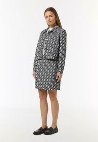 Schwarz-weiße gemusterte Jacke und Rock im Set, mit einem verkürzten Design, Reißverschlusspunkte und runden Formen im Stoff. Schwarze Slipper.