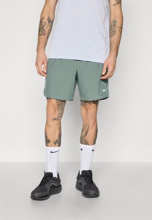Green Nike shorts with a smooth, lightweight fabric, paired with white crew socks featuring black accents and black athletic shoes.