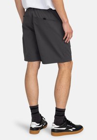 Graue Shorts mit einem elastischen Bund, Gesäßtaschen und einem lockeren Schnitt. Getragen mit schwarz-weißen Sneakers und schwarzen Socken.