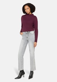 Burgundowy sweter z golfem w połączeniu z wysokim stanem, jasnoszare jeansy i czarne, szpiczaste botki, cechujące się wąskim krojem i teksturowaną tkaniną.