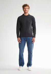 Pull en charbon à col rond et poignets côtelés associé à un jean bleu. Le modèle porte des baskets blanches ; tissu lisse avec une texture en tricot.