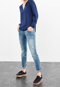 Mörkblå blus med lång ärm och veckade detaljer, matchad med urtvättade ljusblå jeans och svarta sneakers med ljusbrun sula.