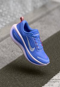 Μπλε αθλητικά παπούτσια Nike με υφή διχτυωτού επάνω τμήματος, ασημένιο λογότυπο και ροζ λεπτομέρειες. Διαθέτουν ορατή σόλα με απορρόφηση ZoomX για άνεση.