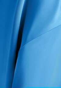 Tessuto blu con una drappeggiatura liscia e leggere ombre, che mostrano la texture e le pieghe in dettaglio ravvicinato.