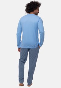 Hellblaues Langarmshirt, kombiniert mit gemusterten blauen Schlafanzughosen. Der Stoff ist weich, und die Hosen weisen ein geometrisches Design auf.