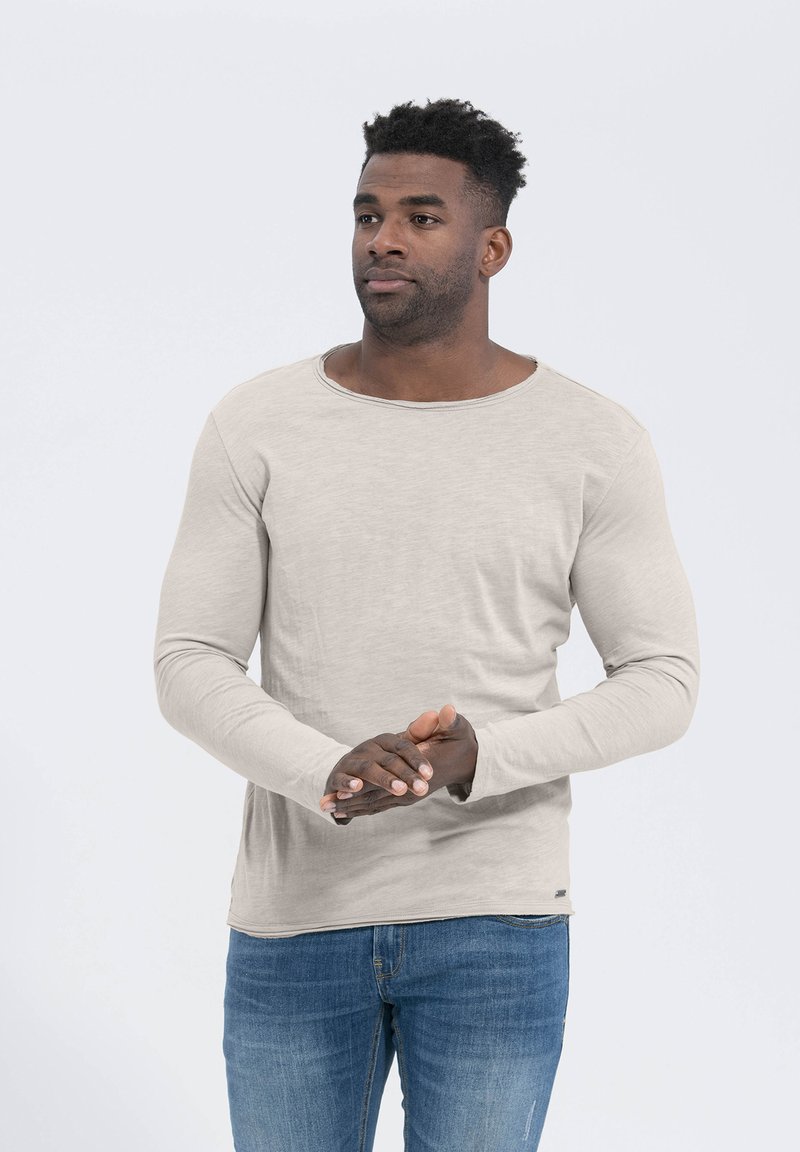 Langärmliges Shirt in hellbeige, aus weichem Stoff mit rundem Halsausschnitt und enganliegenden Ärmeln, kombiniert mit blauen Jeans.