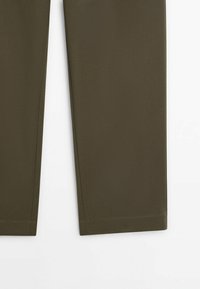 Gros plan sur des jambes de pantalon droites vert olive avec ourlets nets sur fond blanc uni. Aucun motif ou détail visible.