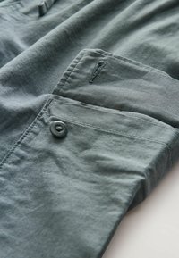 Cotton shirt in soft, muted green with a button closure, featuring a patch pocket and subtle texture, laid flat against a light background.