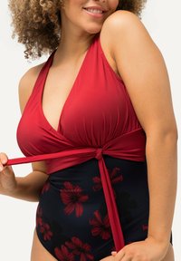 Maillot de bain rouge à encolure halter avec un lien noué à la taille ; présente un motif floral rouge sur un fond bleu foncé. Matériau doux et extensible.