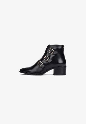 Bottine en cuir noir avec trois boucles décoratives, bout pointu et talon compensé. Texture lisse avec une finition brillante.